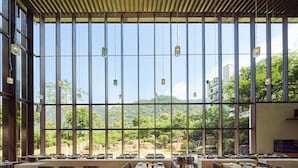 Un vaste espace dédié à la salle à manger, doté de grandes fenêtres offrant une vue sur un paysage montagneux. Les tables sont disposées avec soin et entourées de chaises, et des luminaires suspendus ornent le plafond.