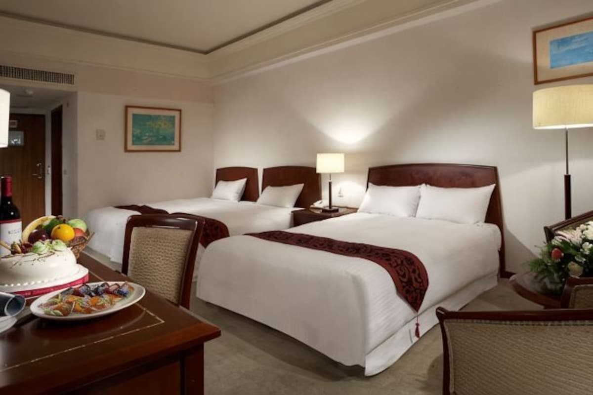 A hotel room with two beds, a dining table with a cake, and a lamp.