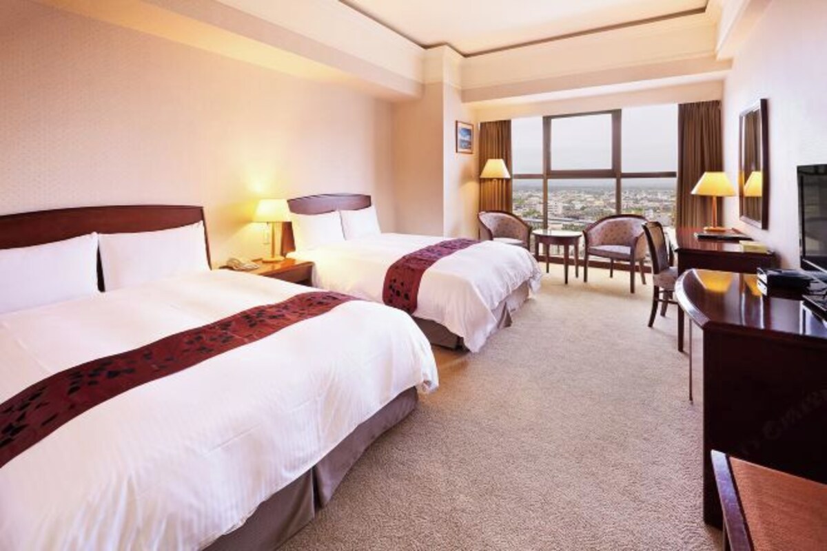 A hotel room with two beds, a desk, a chair, and a TV.
