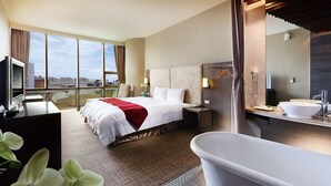A modern hotel room with a large bed, a sitting area with a desk and chair, a bathroom with a freestanding bathtub, and a city view. - Kavalan Hotel (Luodong)