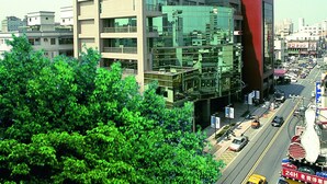 A multi-story hotel with a modern glass facade, a red and beige exterior, and a busy street with cars and taxis below. - Kavalan Hotel (Luodong)