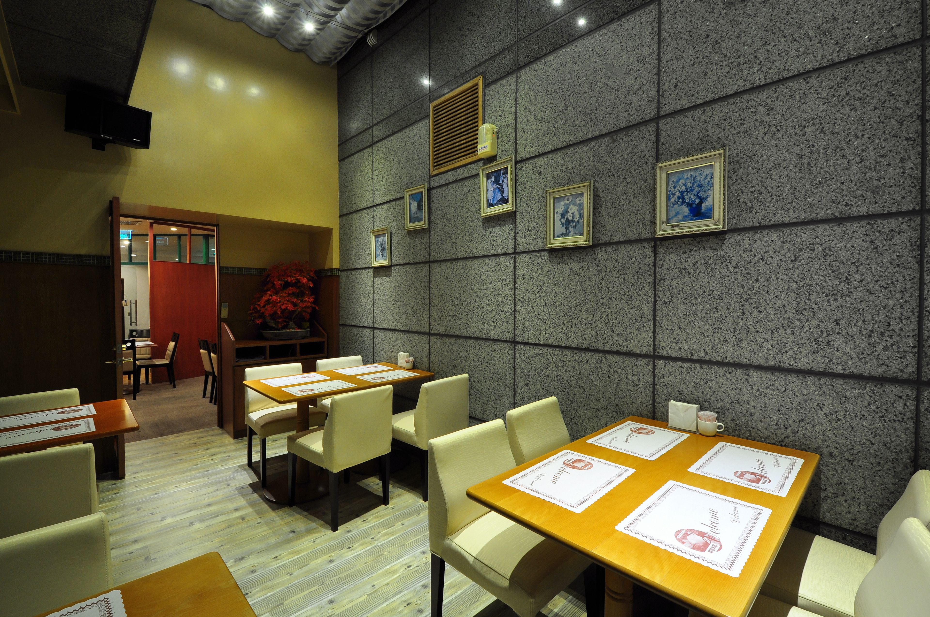 A restaurant with tables and chairs, a wall with framed pictures, and a door leading to another room.