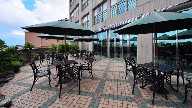 An outdoor patio area with tables and chairs, umbrellas, and a building in the background. - Kavalan Hotel (Luodong)