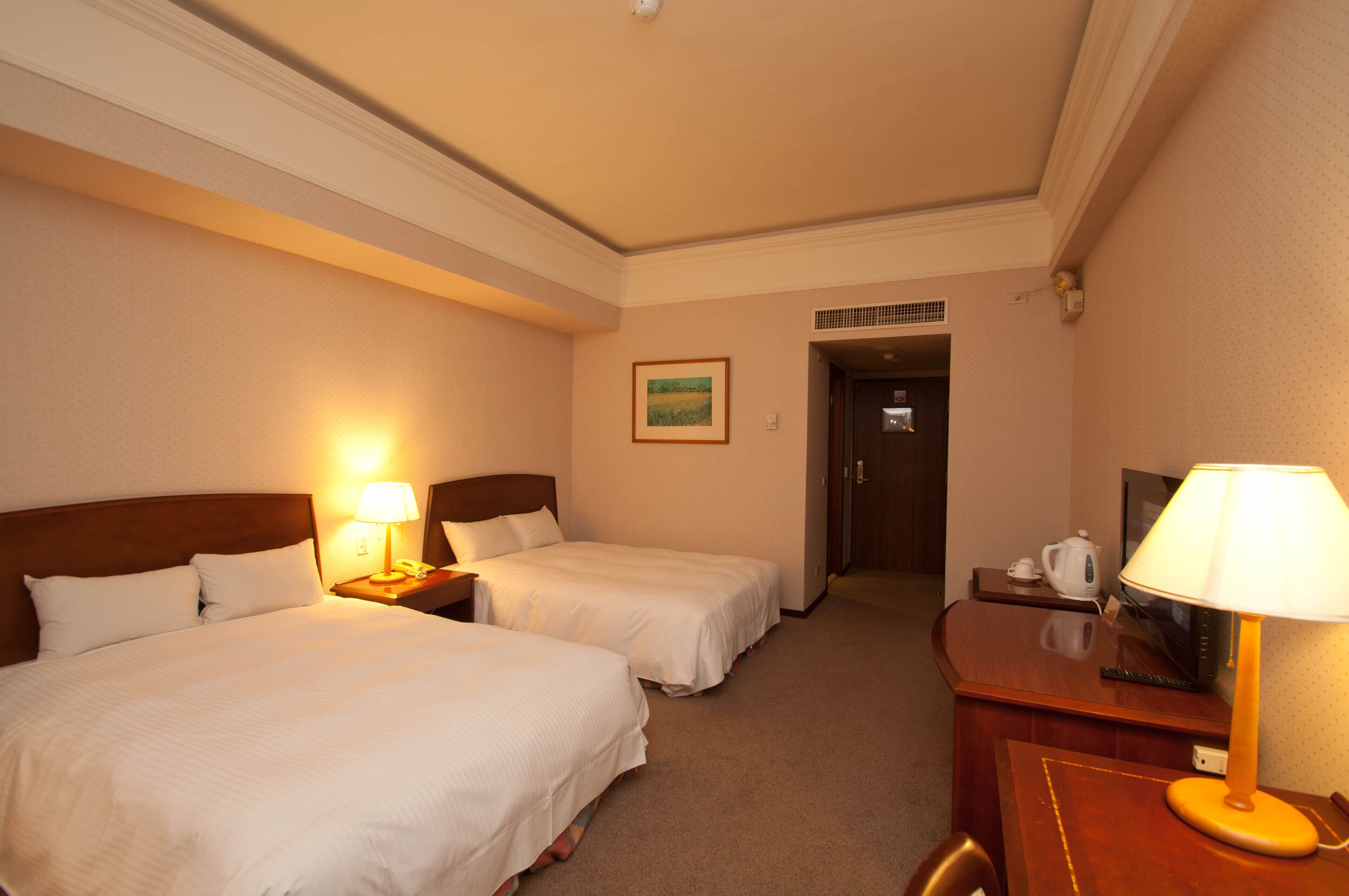 A hotel room with two beds, a desk, a lamp, a television, and a painting on the wall.