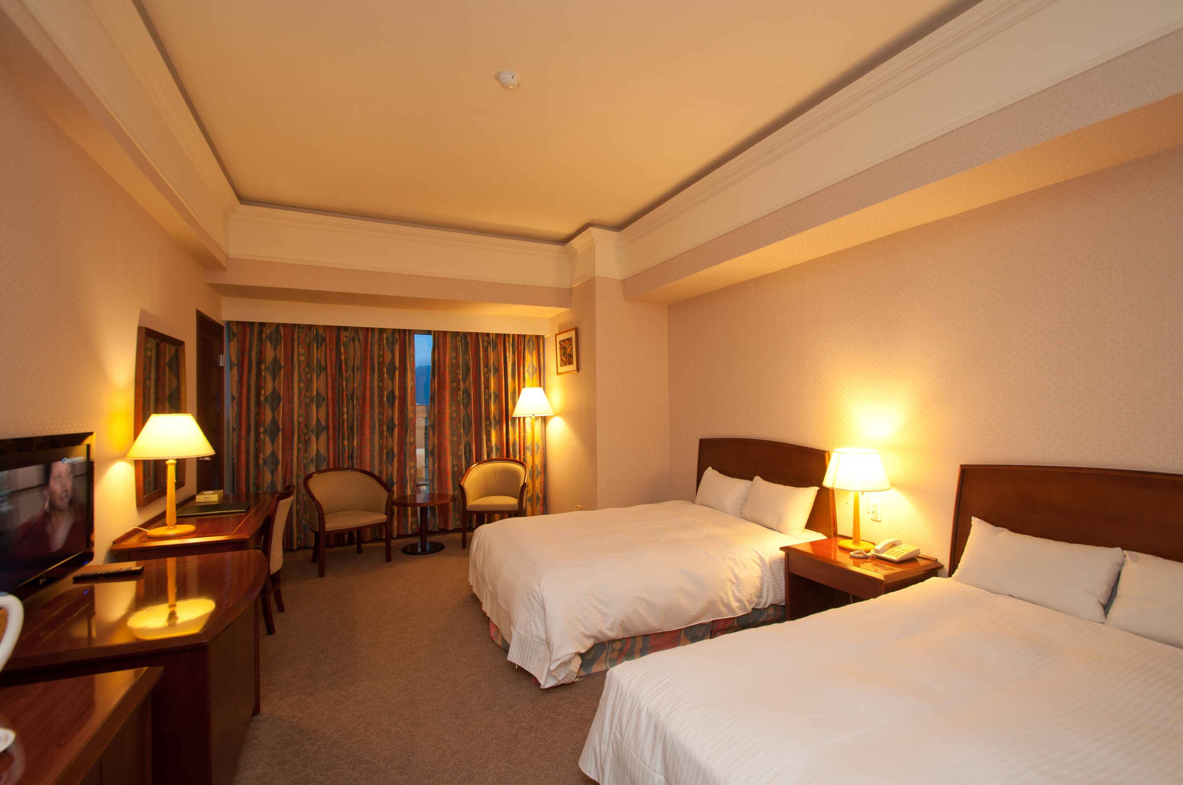A hotel room with two beds, a TV, a desk, and a chair.