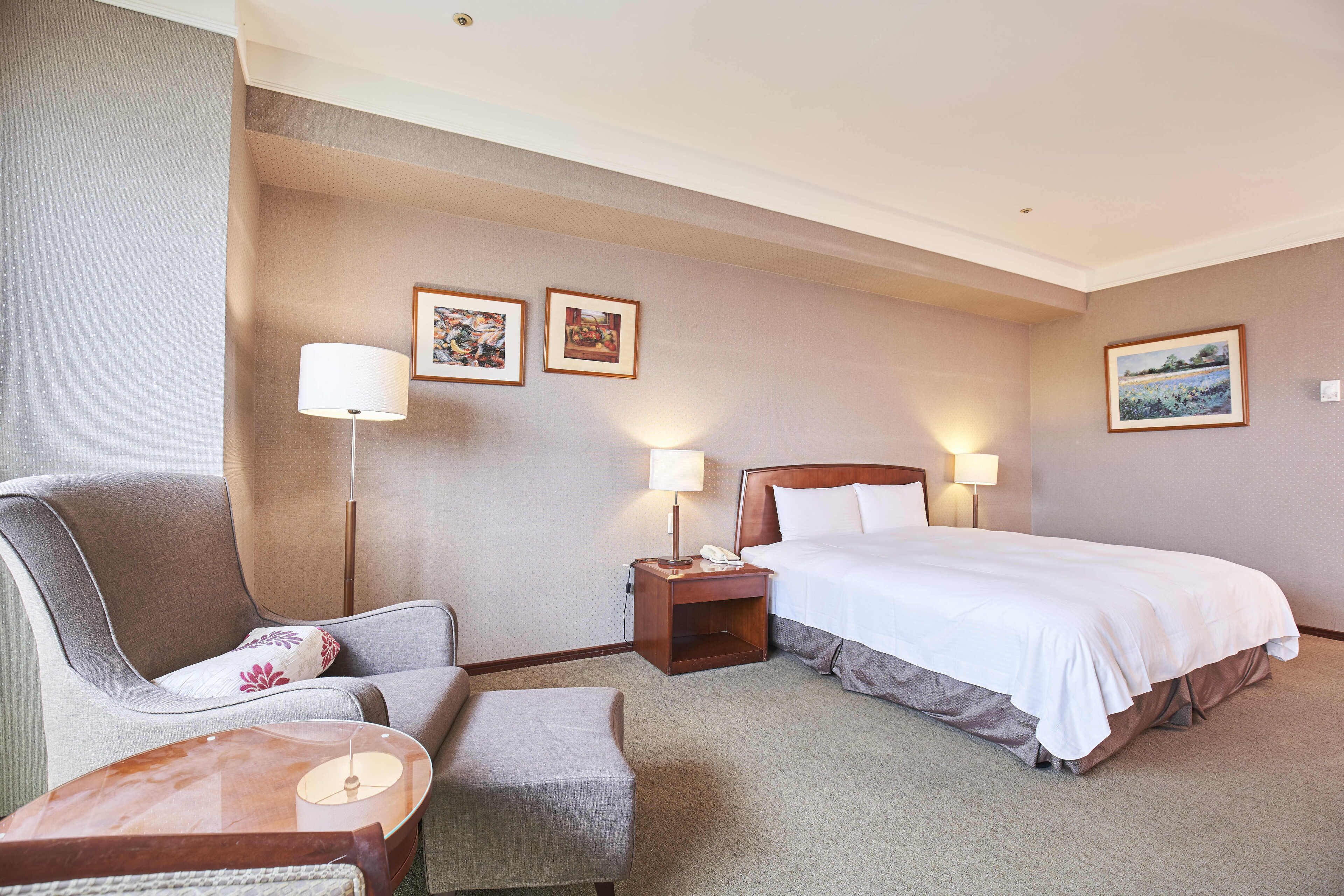 Quarto de hotel com cama, cadeira, escrivaninha e abajur.