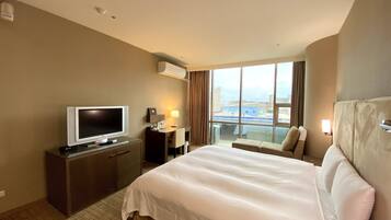 A hotel room with a bed, a desk with a TV, a window with a view, and a ceiling with recessed lighting.