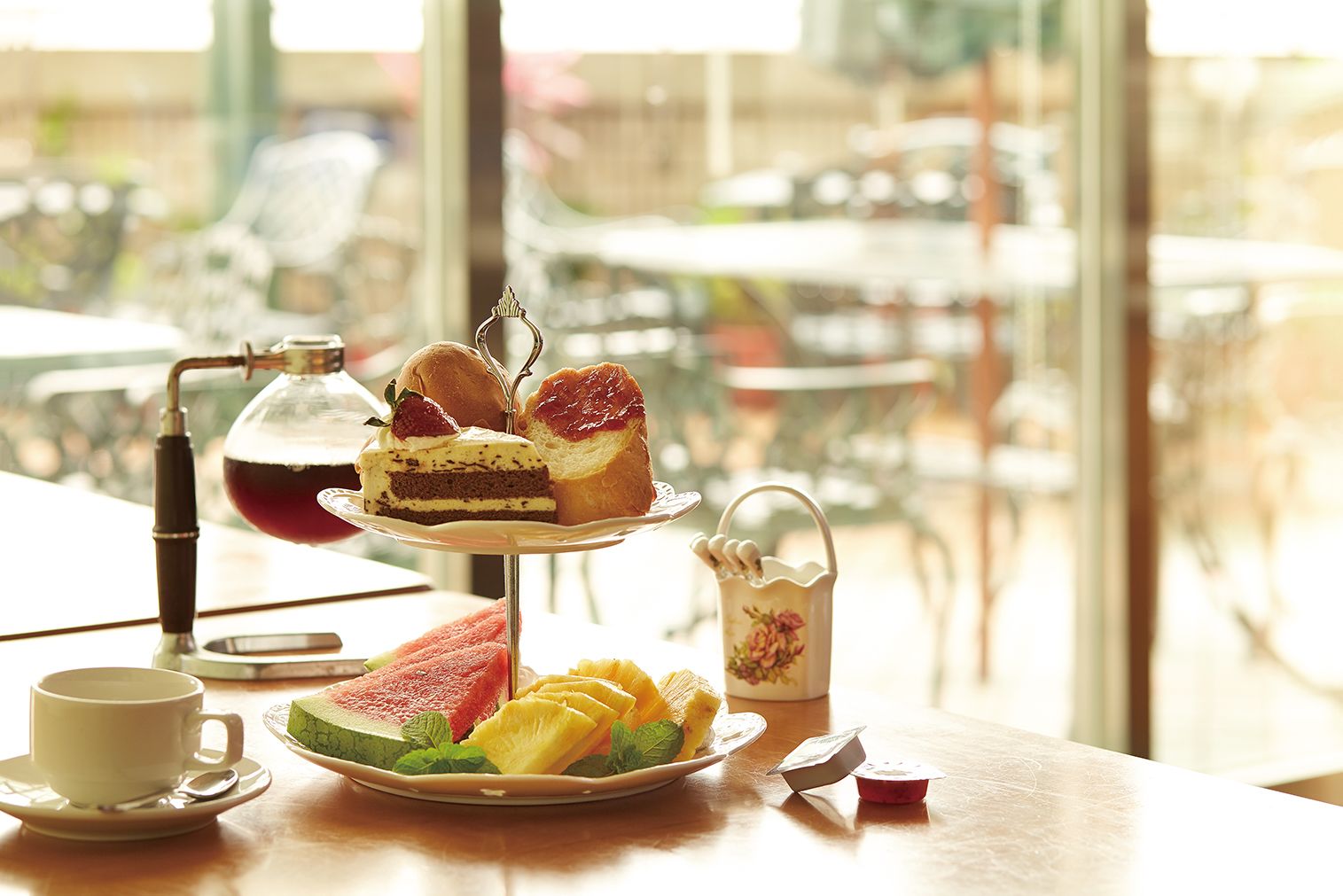 Une table avec un présentoir à étages pour les desserts, une théière, une tasse et une assiette de fruits.