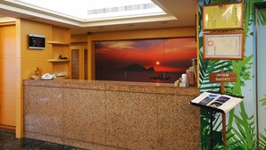 Zona de recepción de hotel con un mostrador de granito, un teléfono en la pared, una pantalla digital y un cartel que indica la disponibilidad de WiFi.