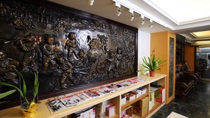 Zona de recepción con una gran pared decorativa, mostrador de recepción con revistas, una planta en maceta y un área de descanso con sillones de cuero.