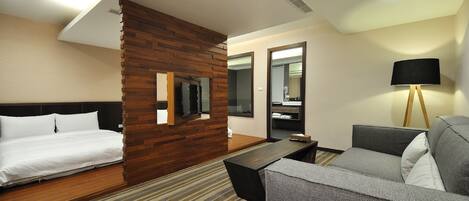 Habitación de hotel con cama, sofá, televisión, pared decorativa de madera, lámpara y espejo.