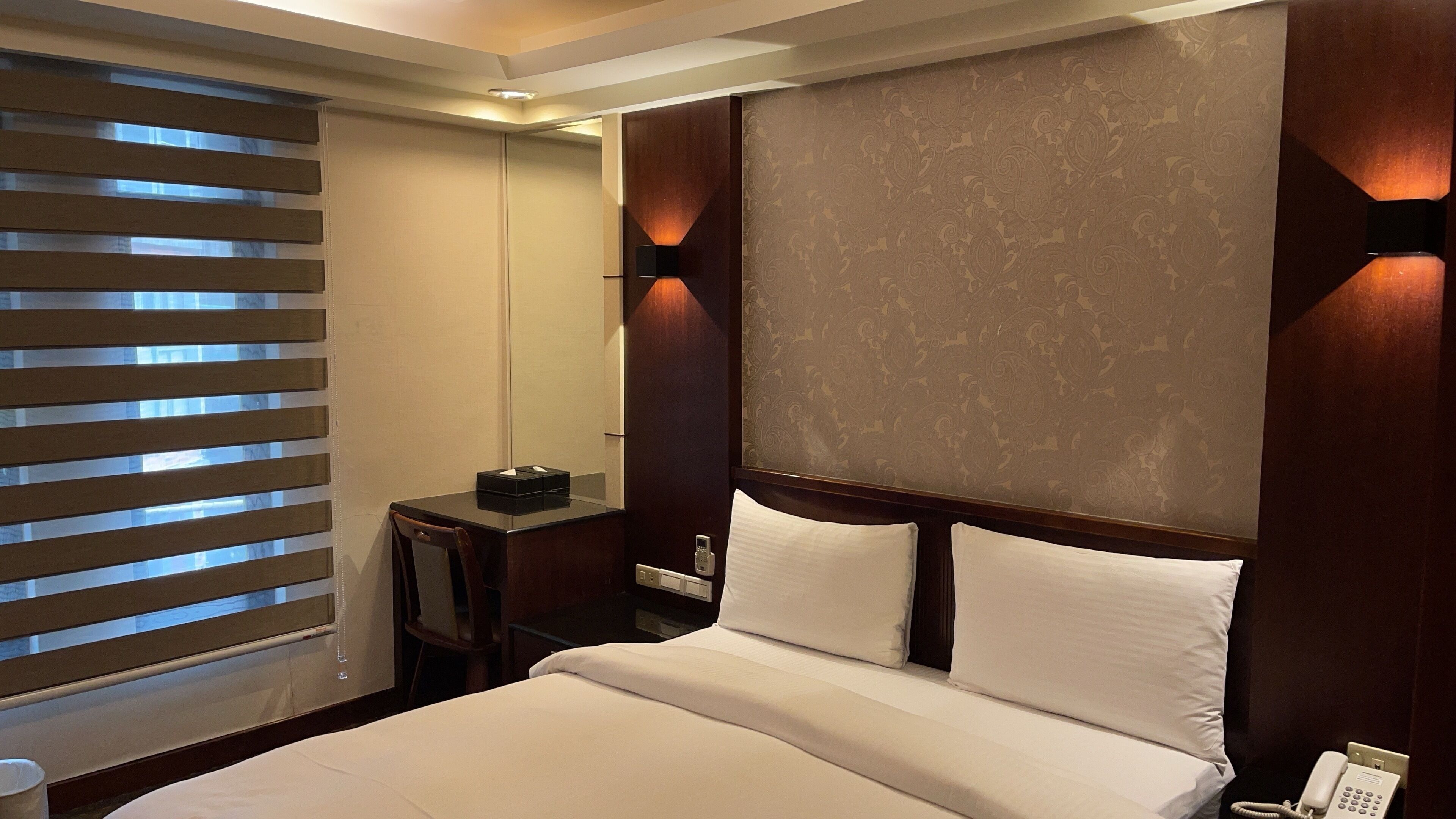 A hotel room with a large bed, a bedside table, a mirror, and a telephone.