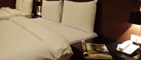 Una habitación de hotel con una cama grande, una mesita de noche con una revista, un teléfono y una lámpara.
