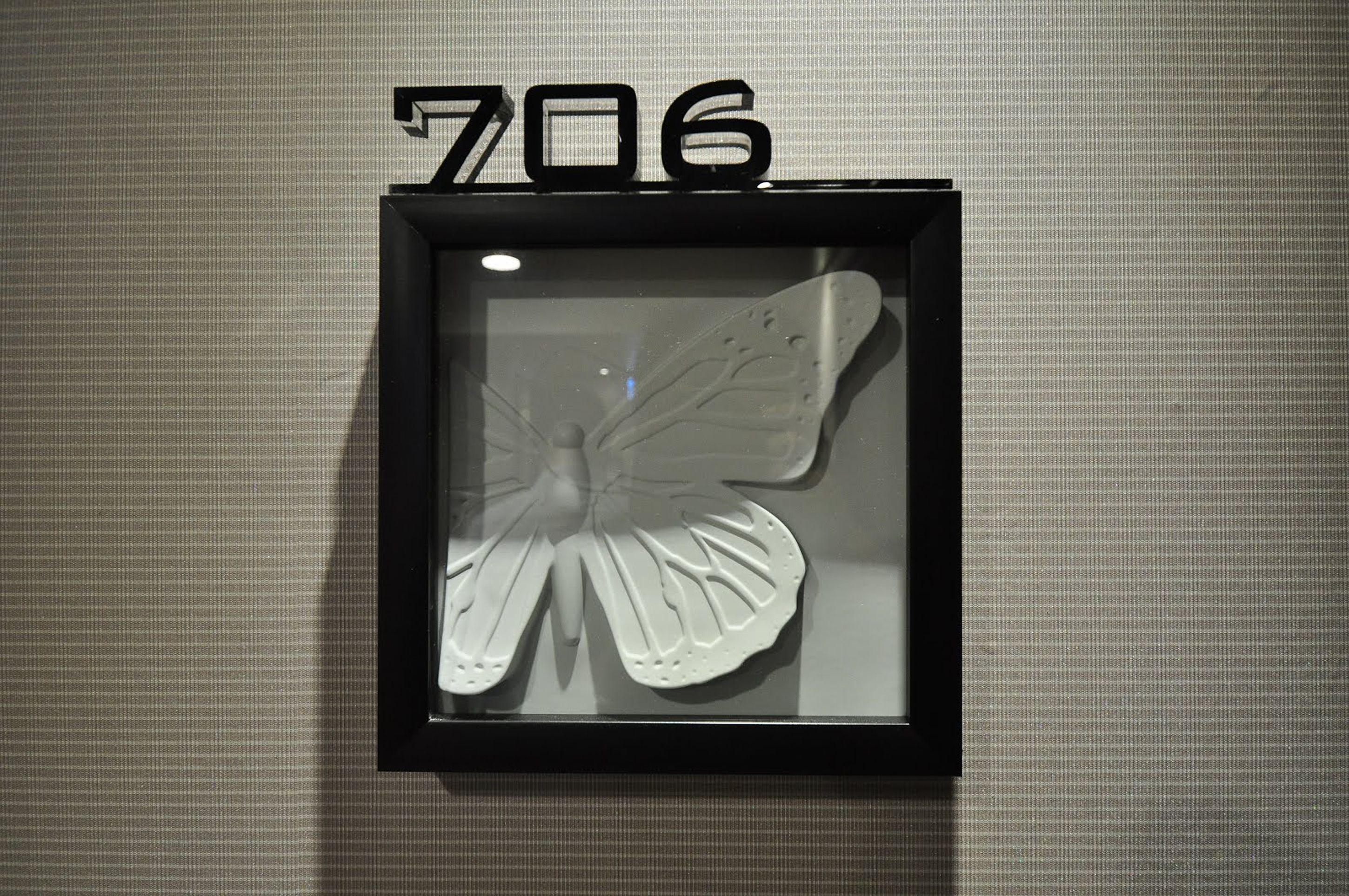 Una obra de arte con mariposas enmarcadas y el número 706 arriba, montada en una pared con textura.