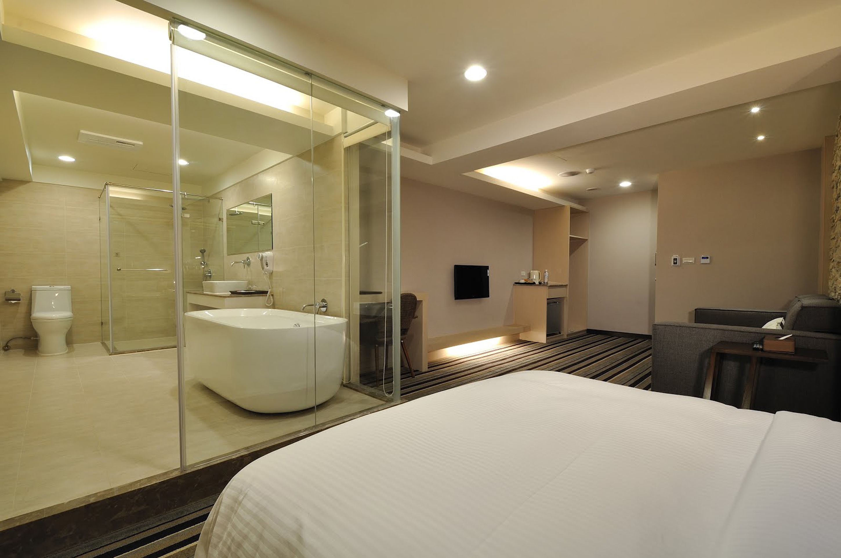 Une chambre d’hôtel moderne dotée d’un grand lit, d’une douche séparée à parois de verre, d’une salle de bain indépendante et d’un coin salon avec un téléviseur à écran plat.
