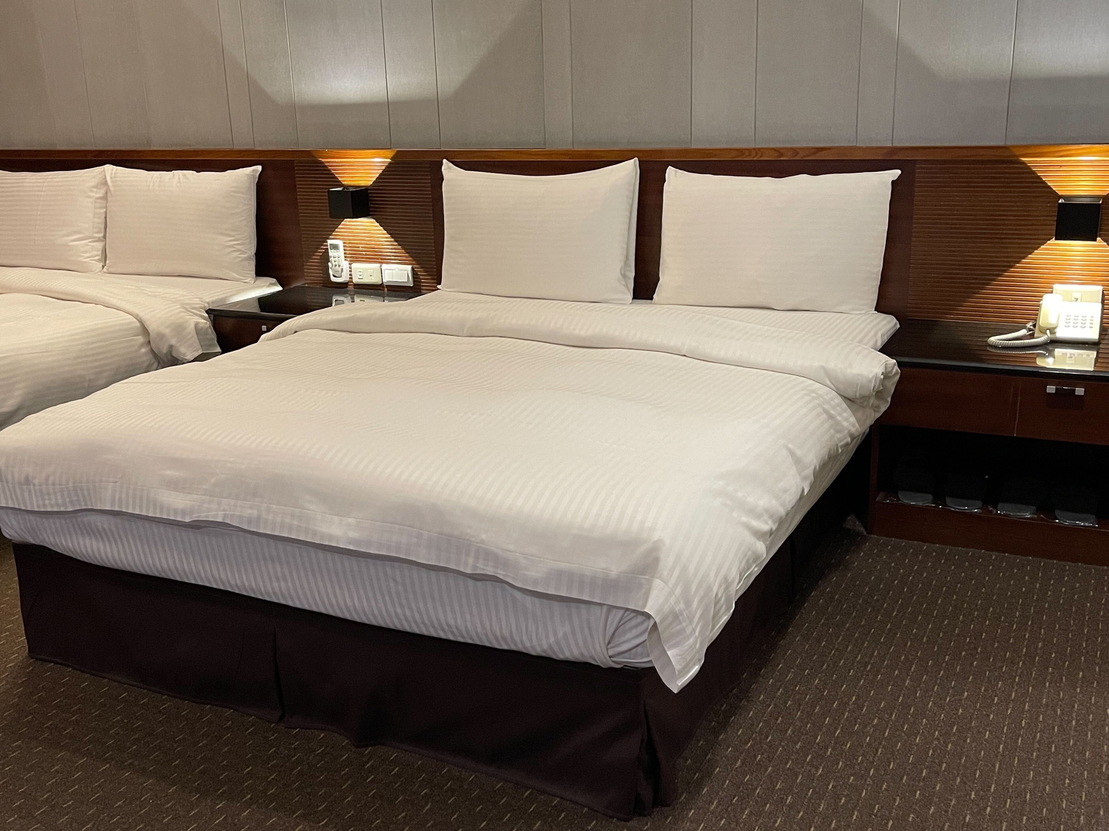 Une chambre d’hôtel avec un grand lit, deux tables de chevet avec des lampes et une petite table avec un téléphone.