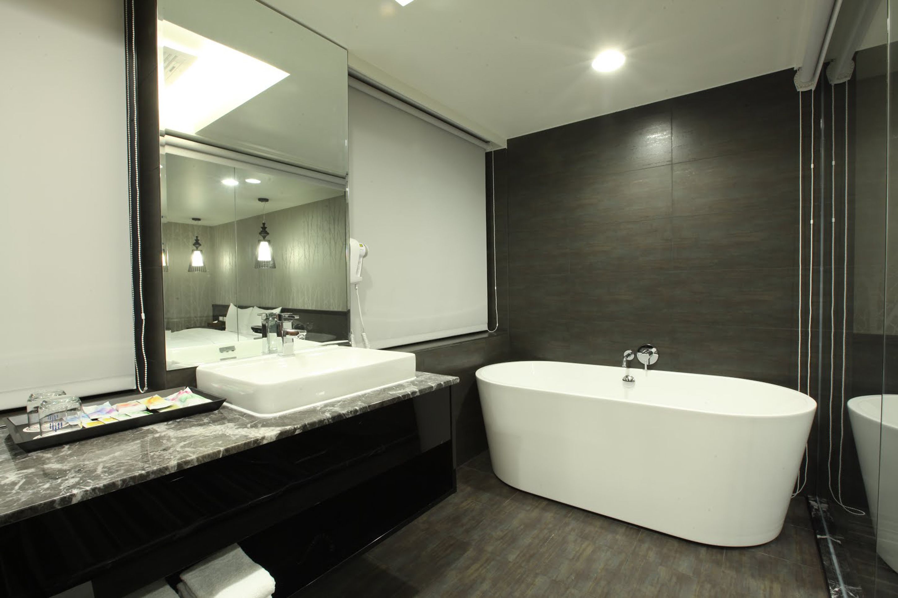 Un baño moderno con un espejo grande, dos lavamanos, una bañera y una pared de madera oscura.