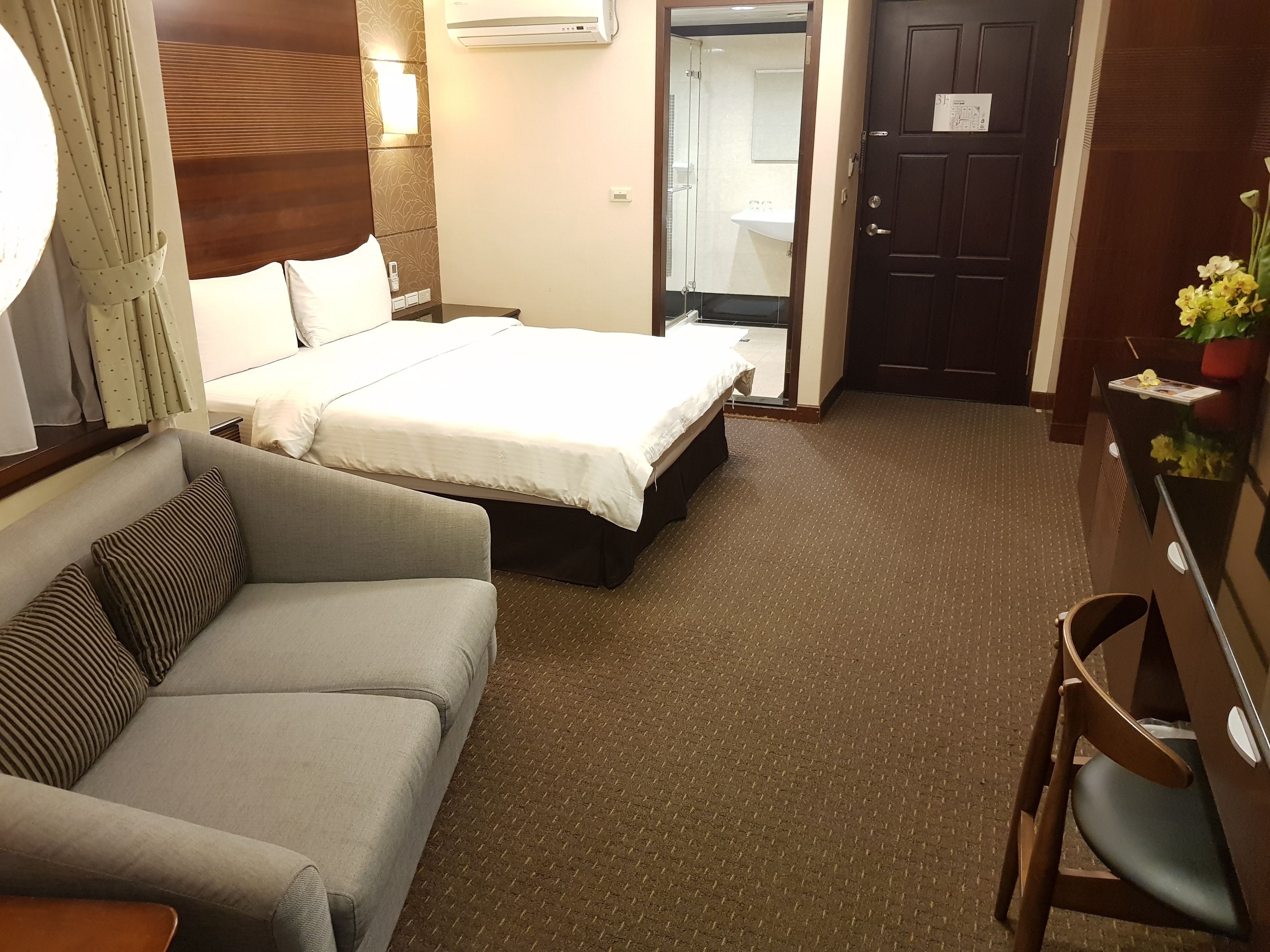 A hotel room with a bed, a sofa, a desk, and a mirror.
