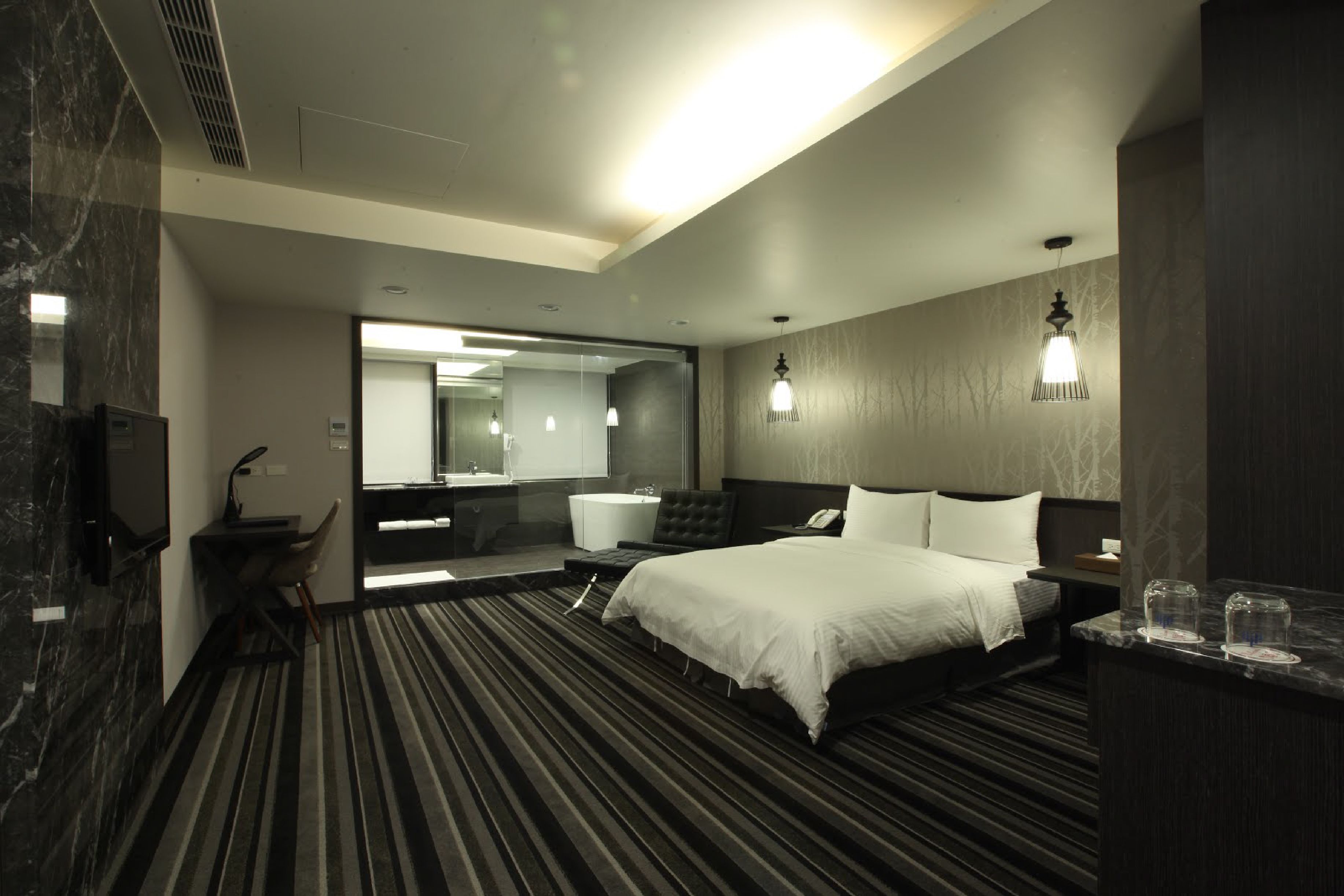 Una habitación de hotel moderna con una cama grande, un escritorio, una silla, un tocador con espejo y un baño con bañera.