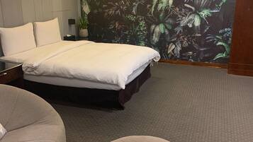 Un dormitorio con una cama, un reposapiés redondo, una mesita de noche y una pared decorada con un mural tropical.