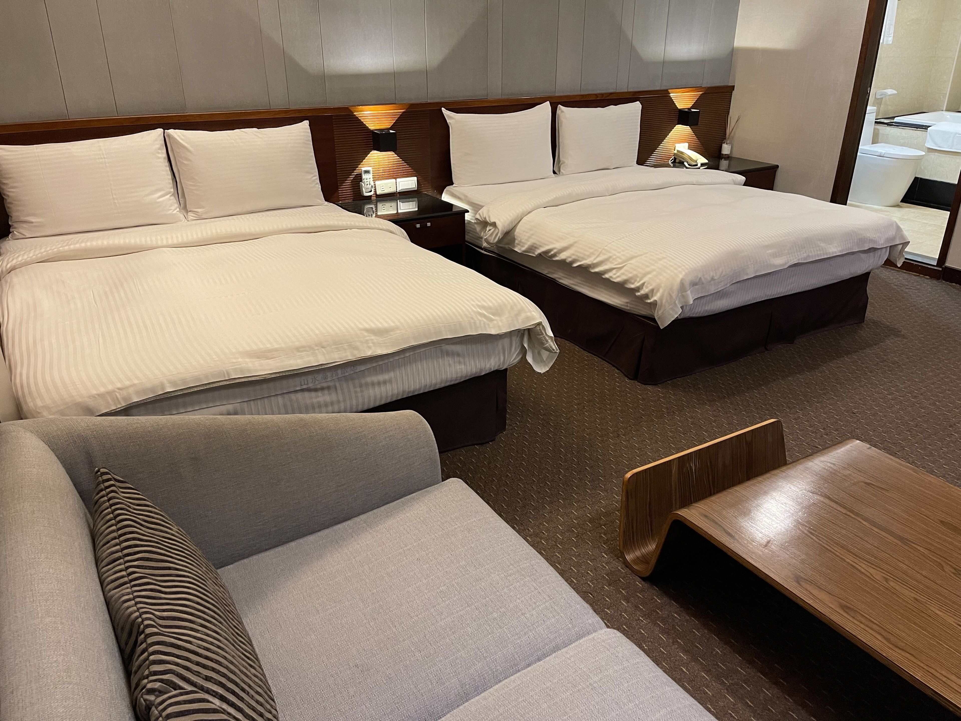 A hotel room with two beds, a sofa, and a wooden table.