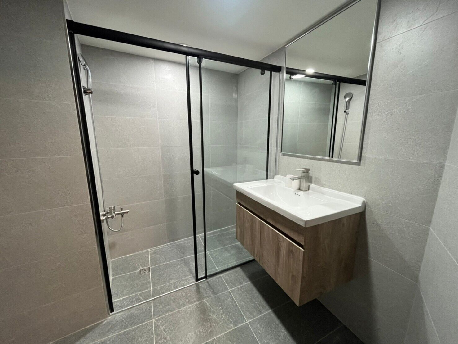 Un bany modern amb plat de dutxa de vidre, un lavabo blanc i un moble de tocador de fusta.