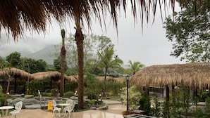 An outdoor seating area with thatched-roof structures, white chairs, and a stone wall. - Yawan Spa Hotel (Beinan)
