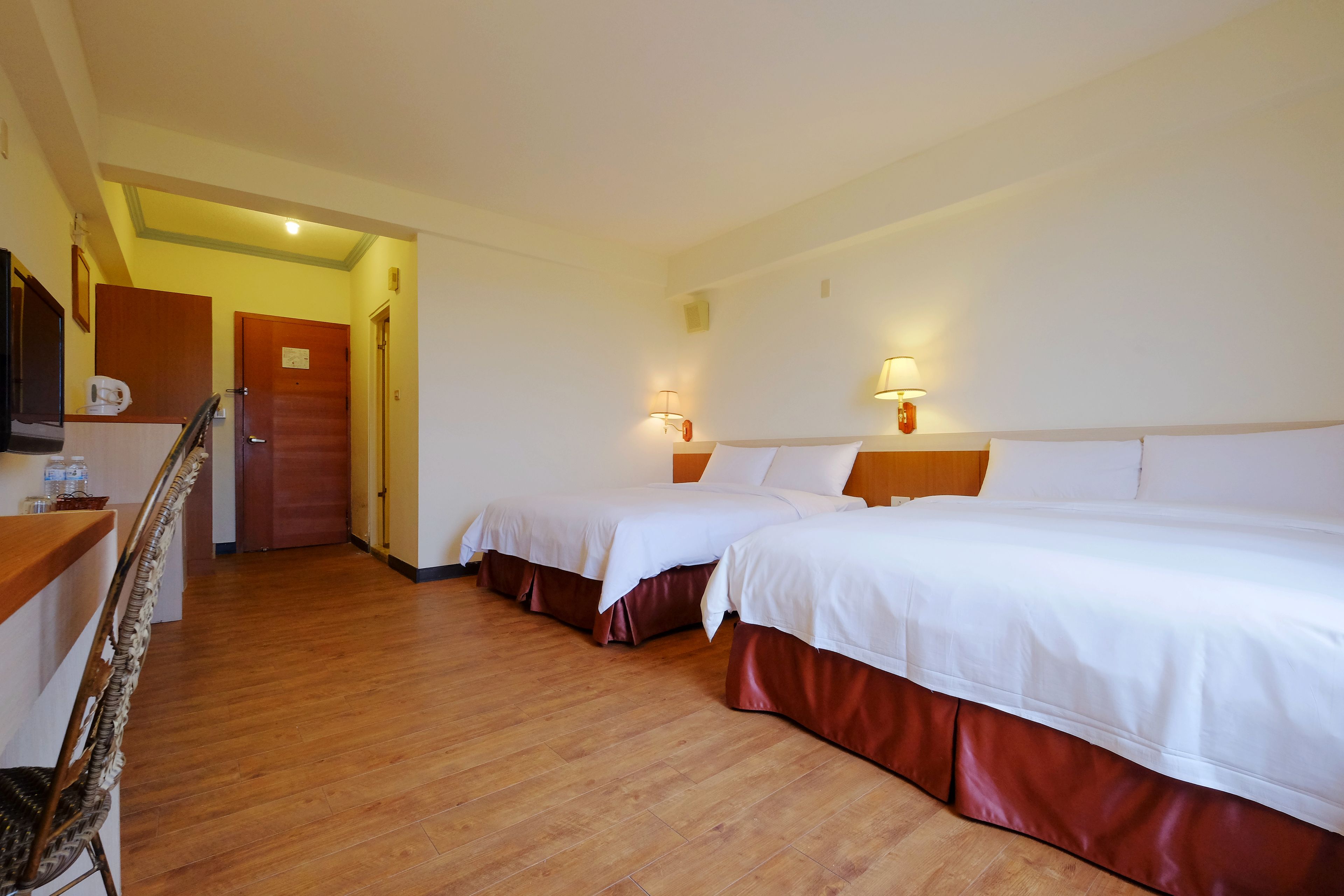 A hotel room with two beds, wooden flooring, a desk with a chair, and a staircase leading to another room.
