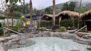 A clear pool surrounded by rocks and a thatched-roof structure. - Yawan Spa Hotel (Beinan)