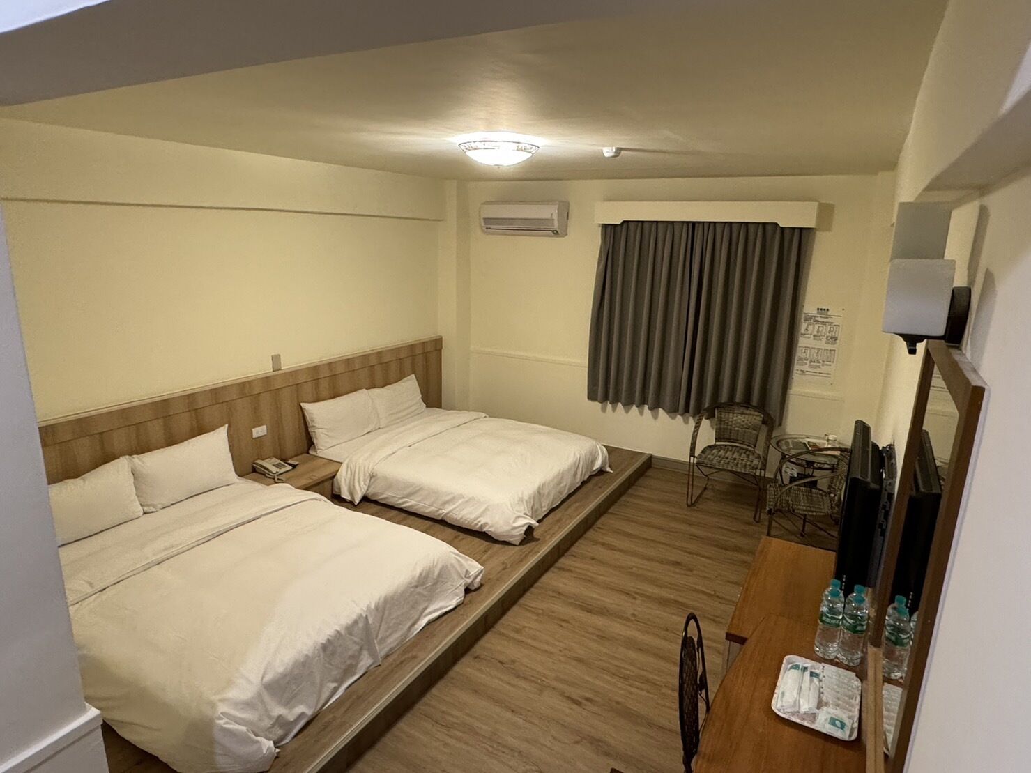 Habitación de hotel con dos camas, un escritorio con silla, televisor y ventana con cortinas.