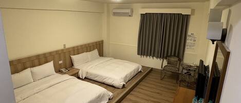 Habitación de hotel con dos camas, un escritorio con silla, televisor y ventana con cortinas.