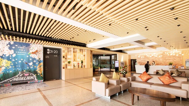 A modern hotel lobby with a reception desk, seating area, and a large floral poster. - Liga Hotel (Hualien City)