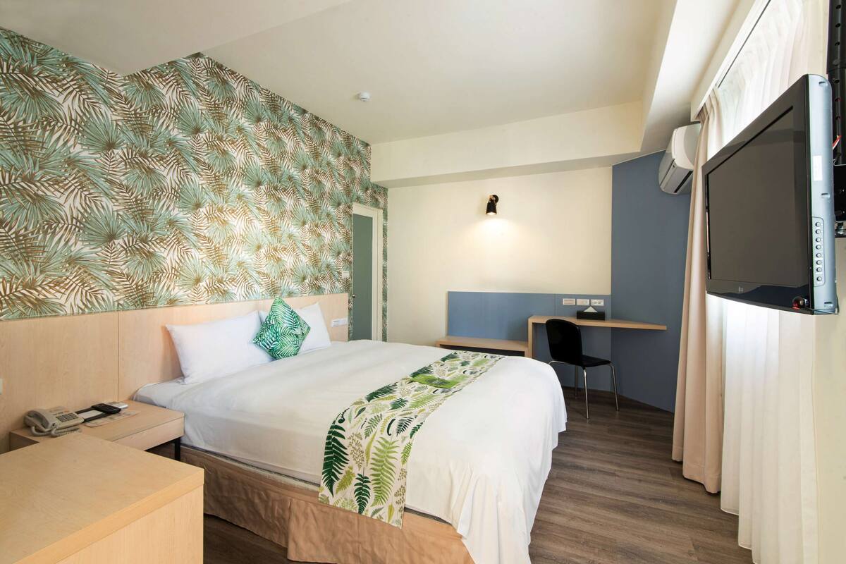 A hotel room with a bed, a desk, a chair, a telephone, and a television.