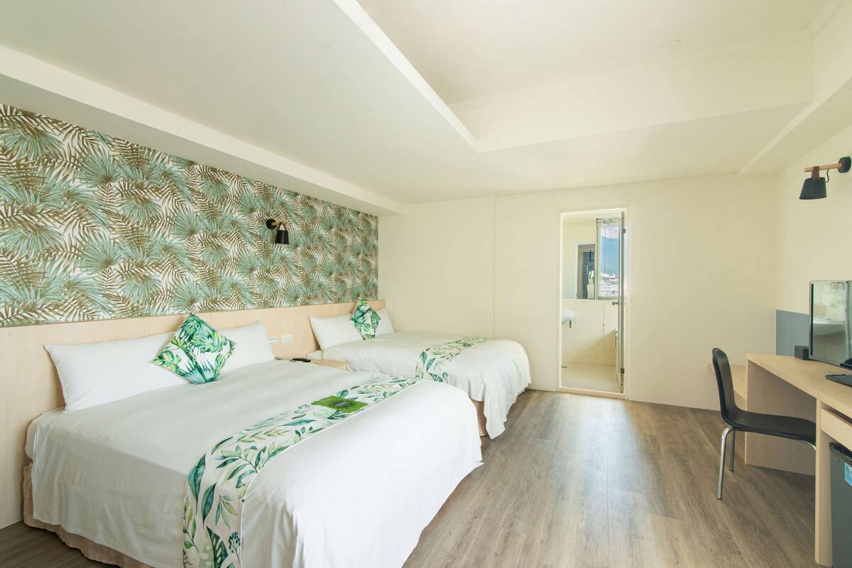 A hotel room with two beds, a desk, and a chair. There is a door leading to another room.