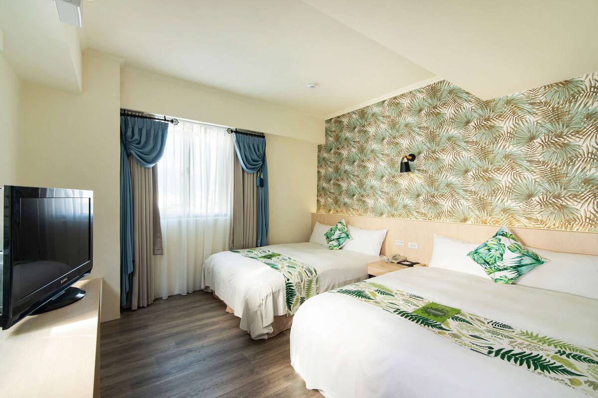 A hotel room with two beds, a TV, and a large window with curtains.