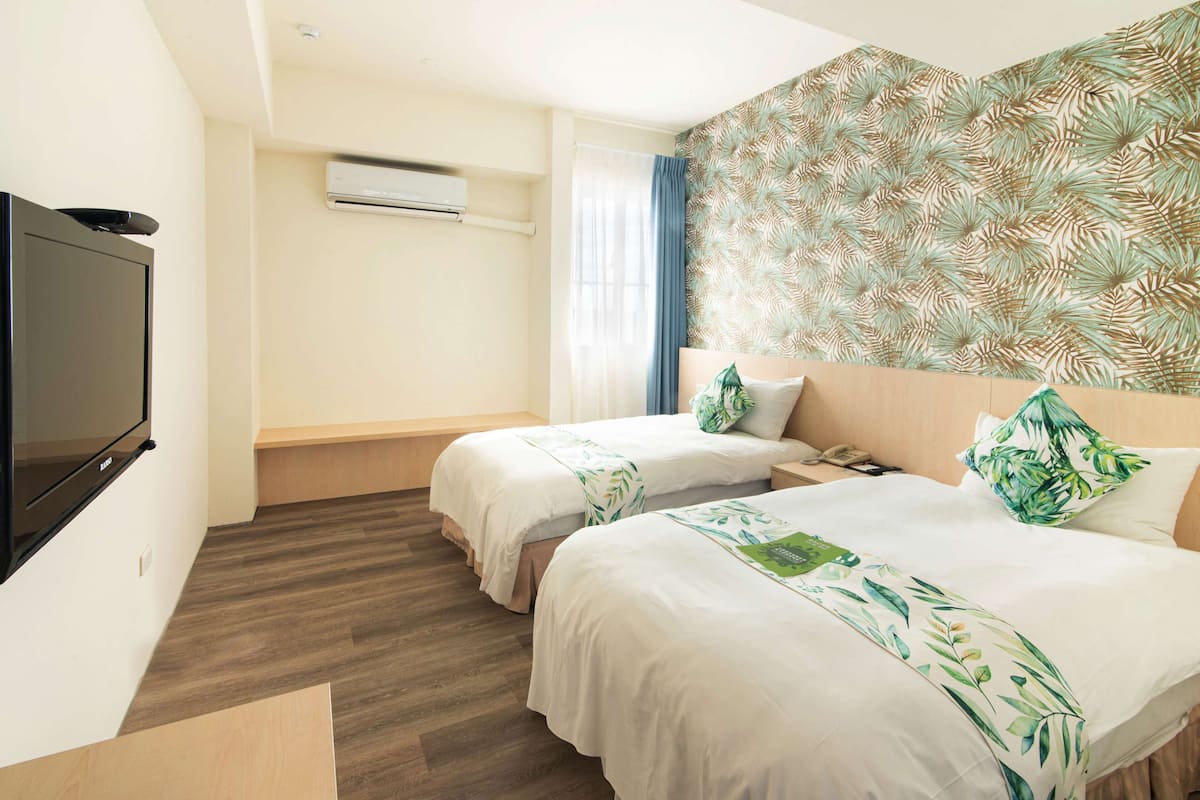 A hotel room with two beds, a flat-screen TV, an air conditioning unit, and a patterned wall.