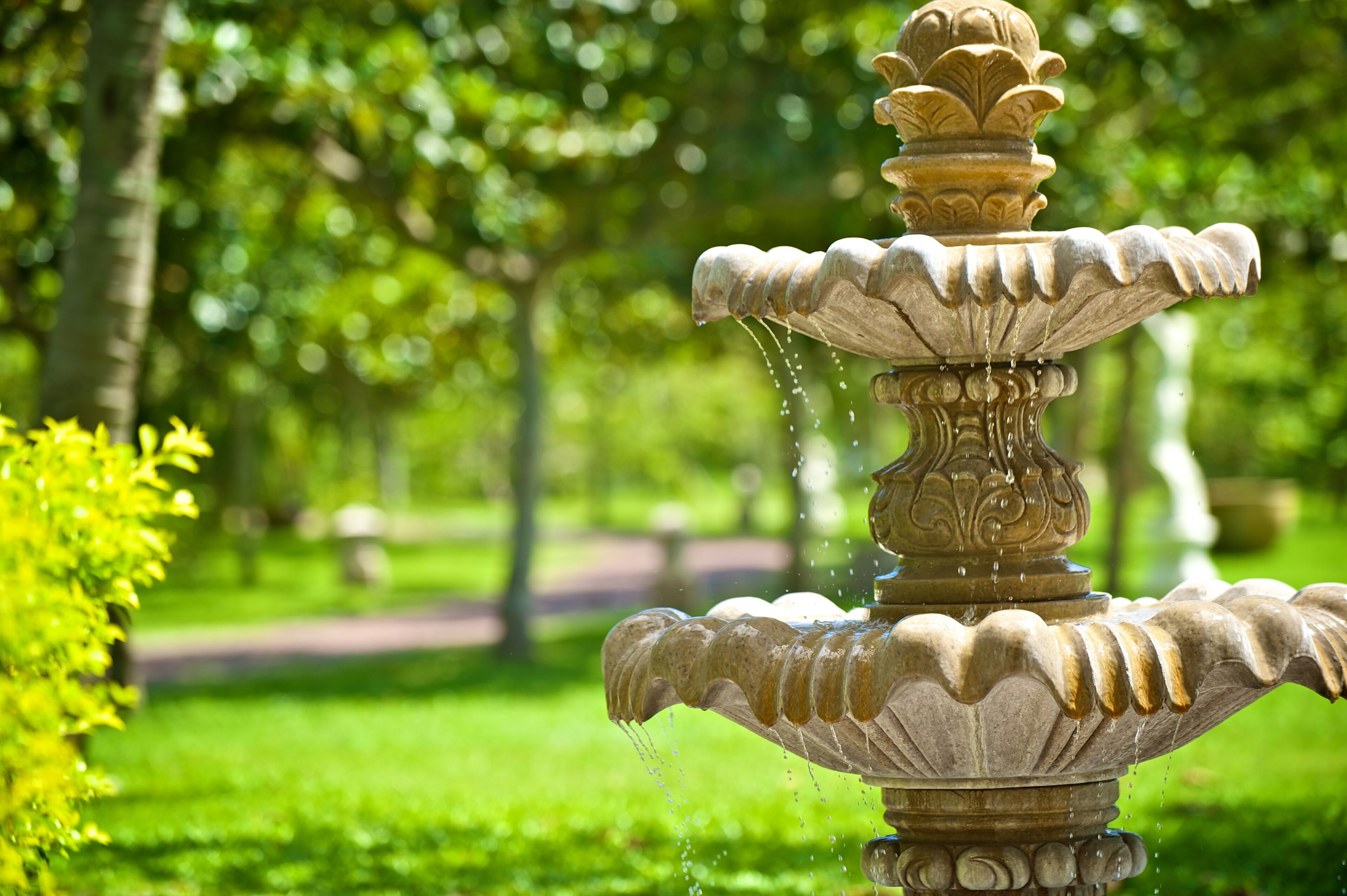 A stone fountain with water spouting from its top tier, set in a lush green park.