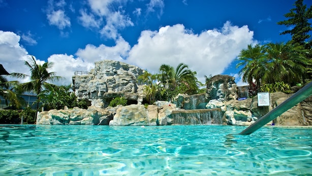 A clear blue pool with a rocky waterfall backdrop and palm trees. - Promisedland Resort & Lagoon (Shoufeng)