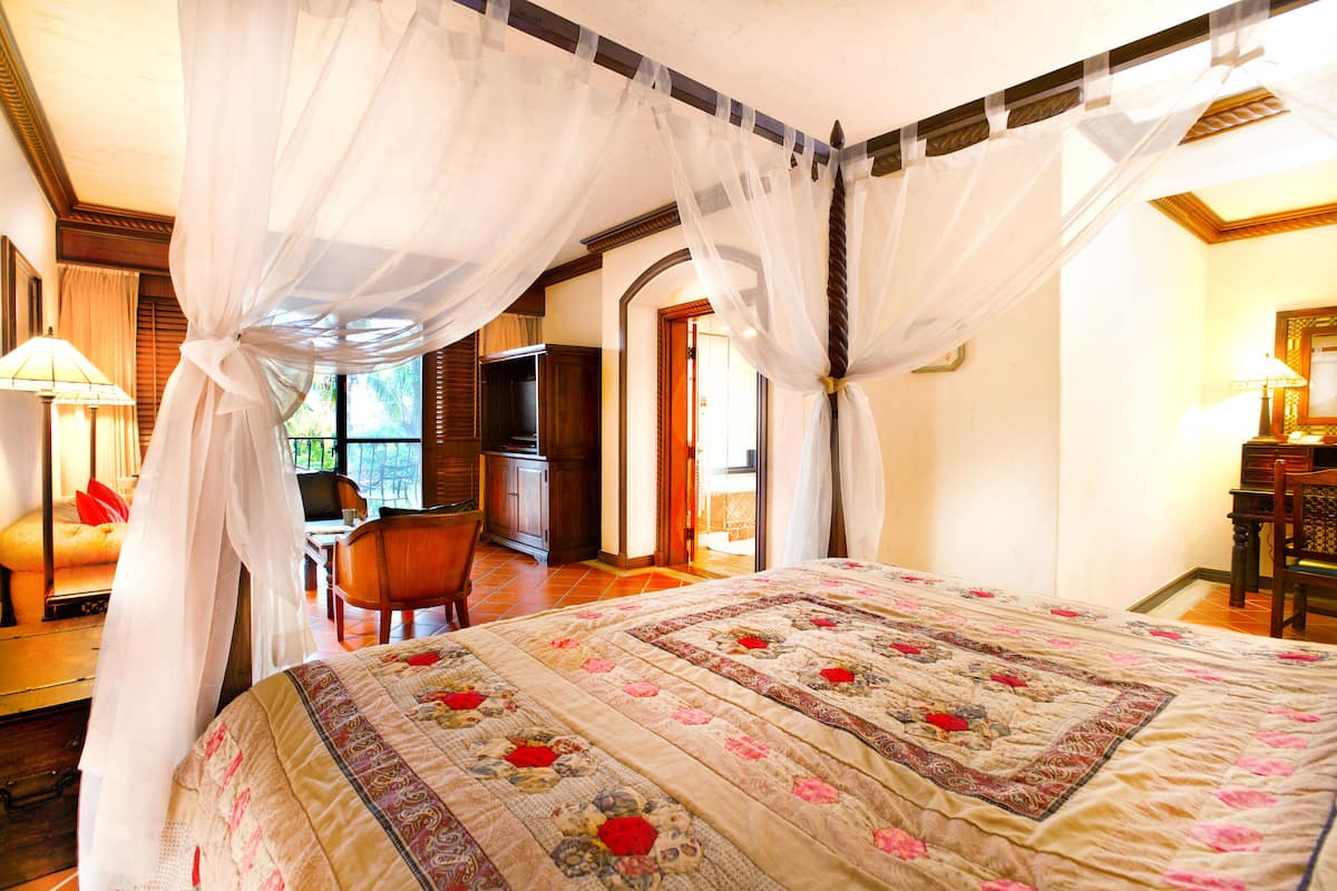 A bedroom with a large bed, a canopy, a desk, and a chair.