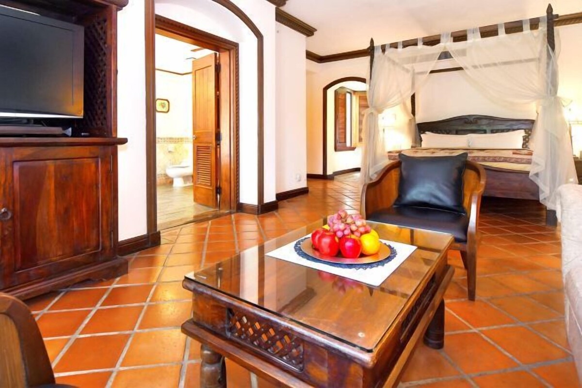 A hotel room with a bed, a television, a dining table with fruit, and a chair.