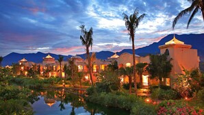 A resort with multiple buildings, a reflective water body, and palm trees. - Promisedland Resort & Lagoon (Shoufeng)
