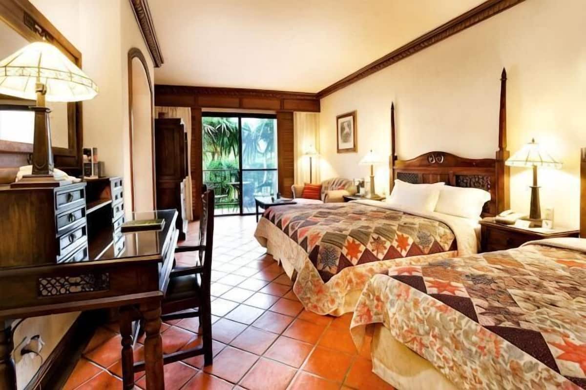A hotel room with a bed, desk, chair, and a view of the outdoors.