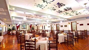 A spacious dining area with multiple tables and chairs, a tiled floor, and decorative ceiling elements.