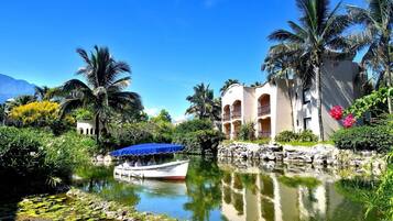 A resort with a water body, a boat, and a building with balconies.