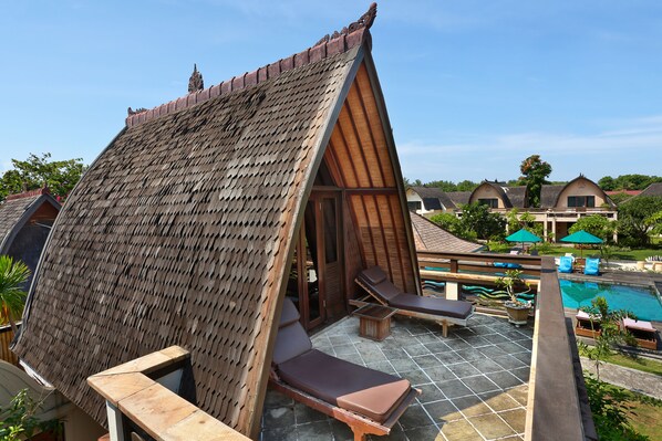 A traditional thatched-roof structure with a pool area, lounge chairs, and umbrellas.