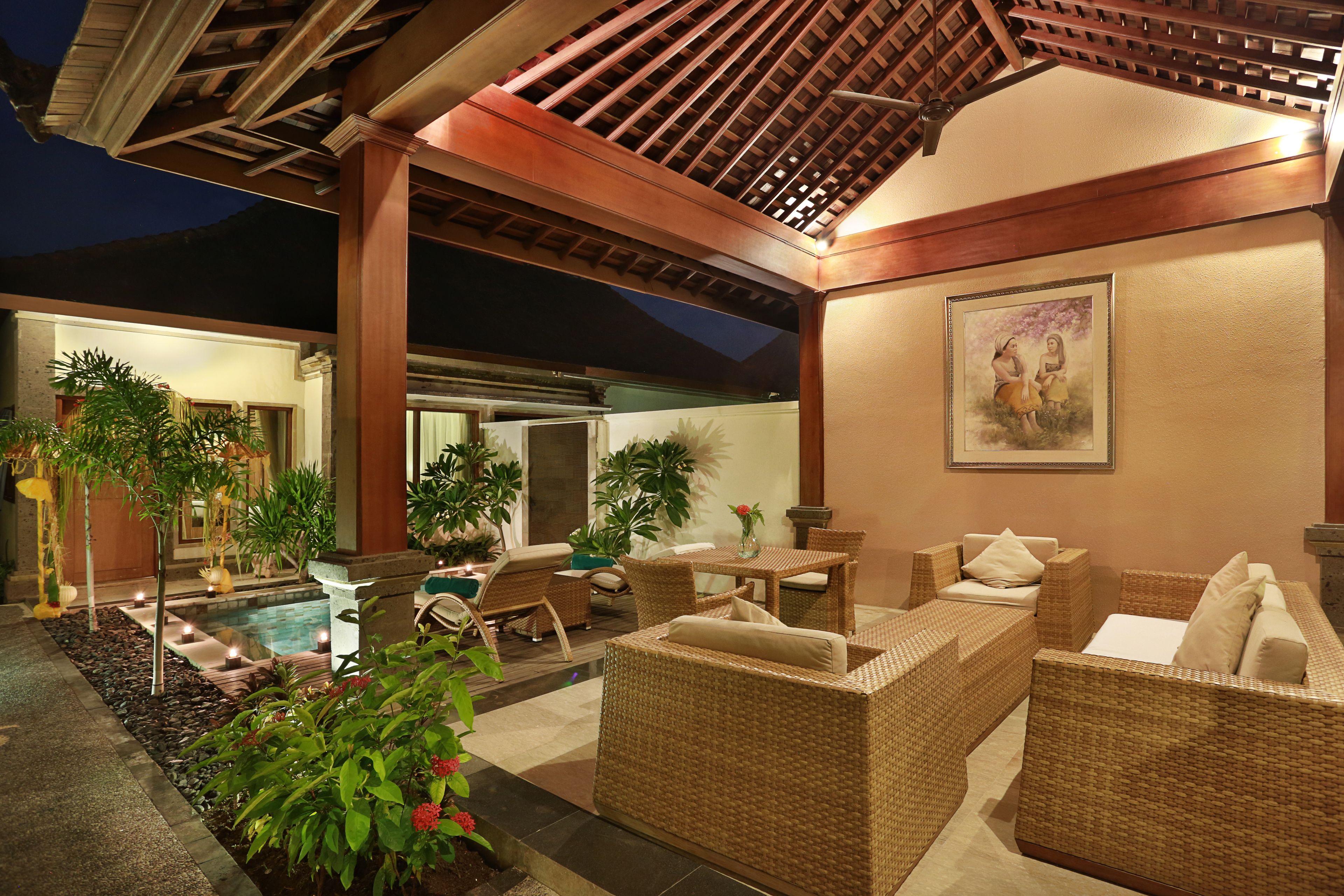 A well-lit outdoor lounge area with wicker furniture, a pool, and potted plants.