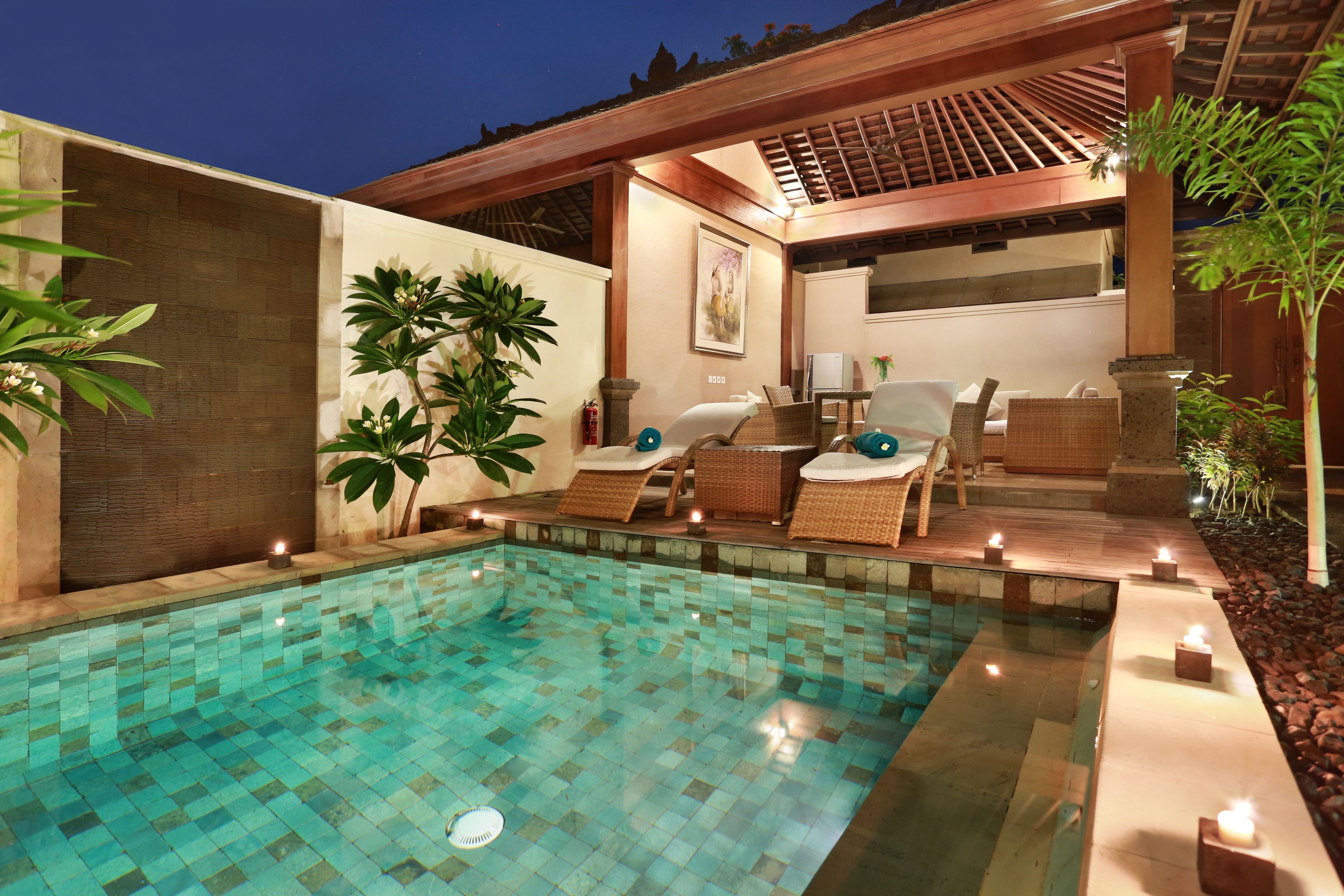 A swimming pool with tiled flooring, surrounded by lounge chairs and a wooden pergola.