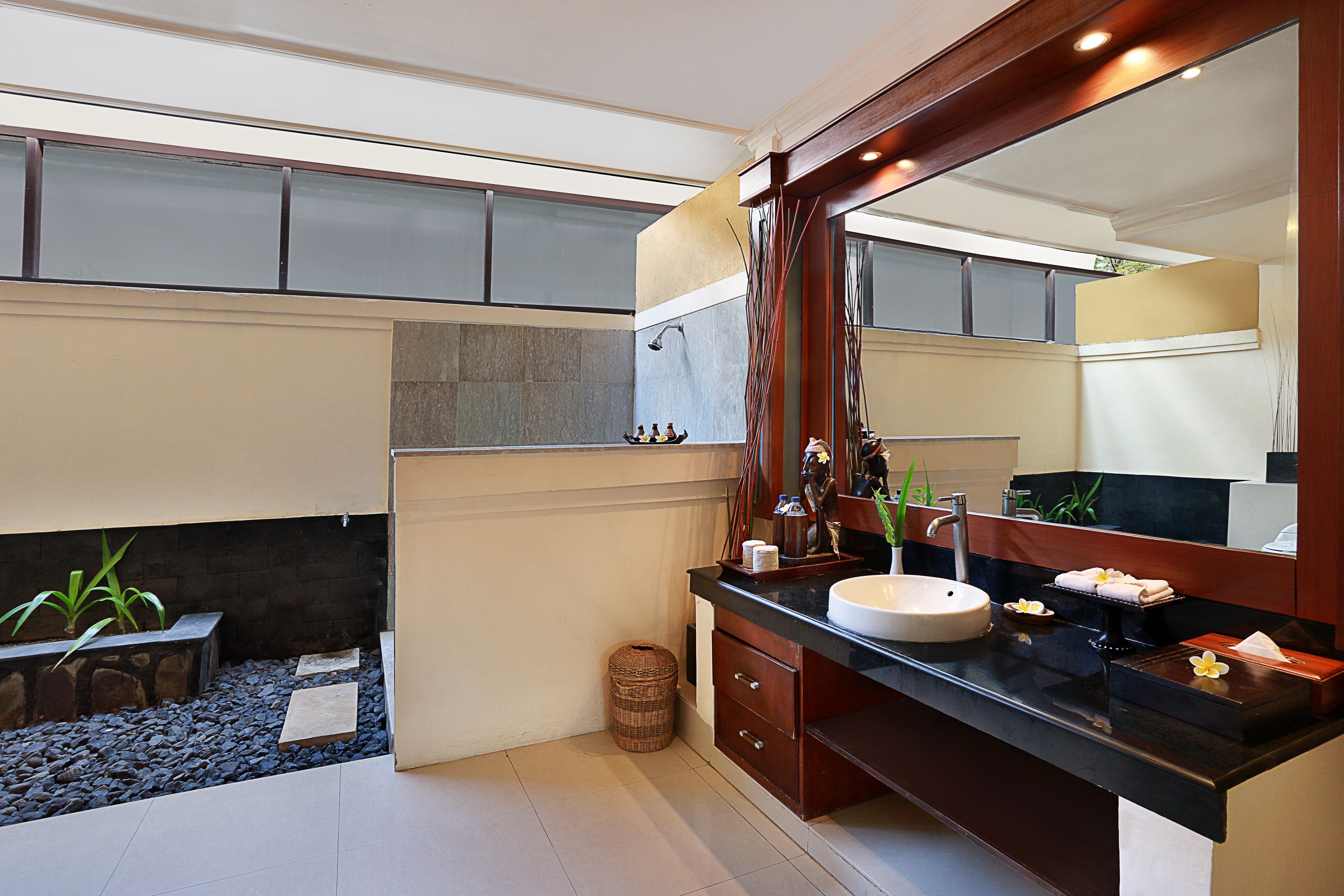 A modern bathroom with a large mirror, a sink, and a small plant area.