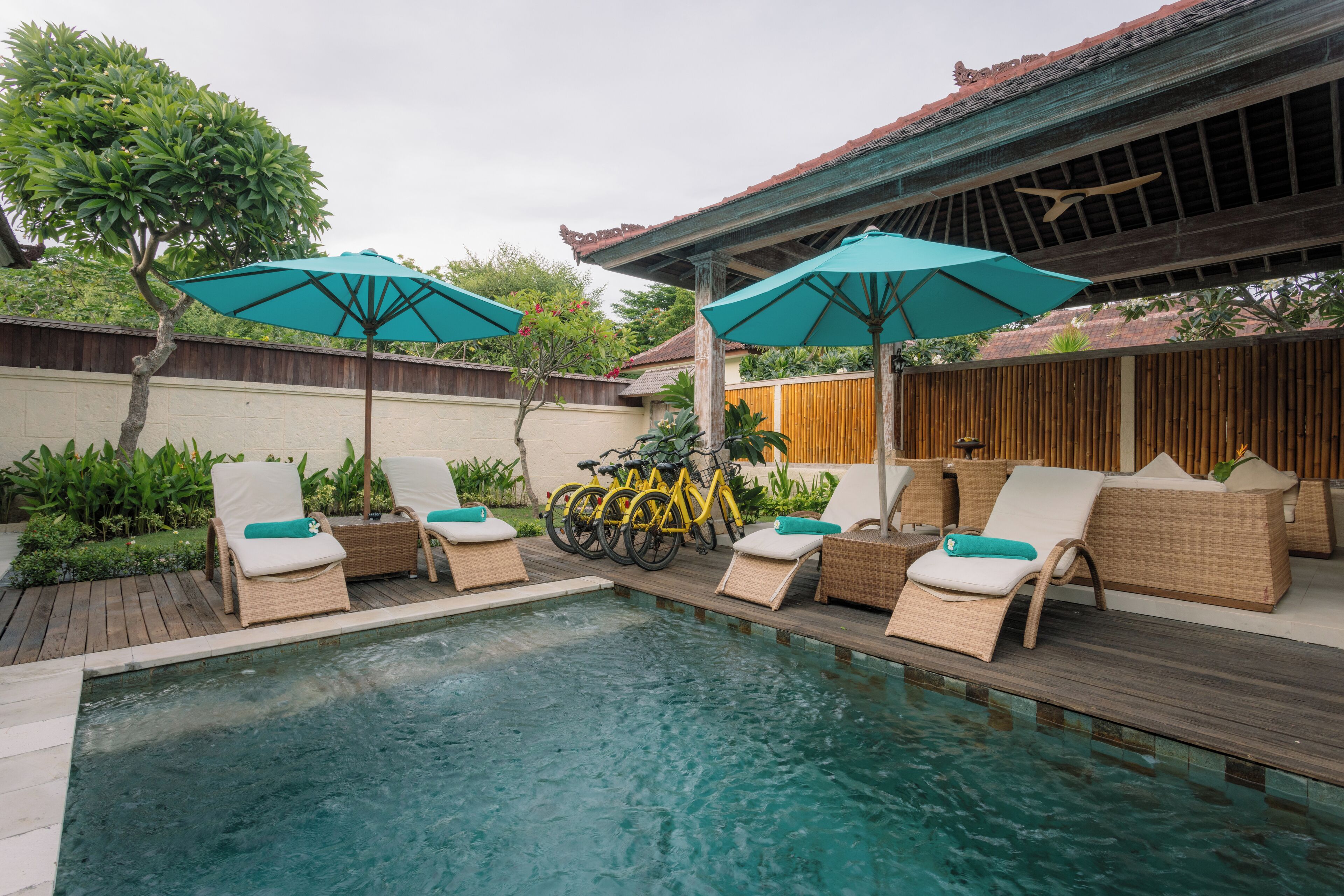 A pool area with lounge chairs and umbrellas, surrounded by wooden fences and greenery.