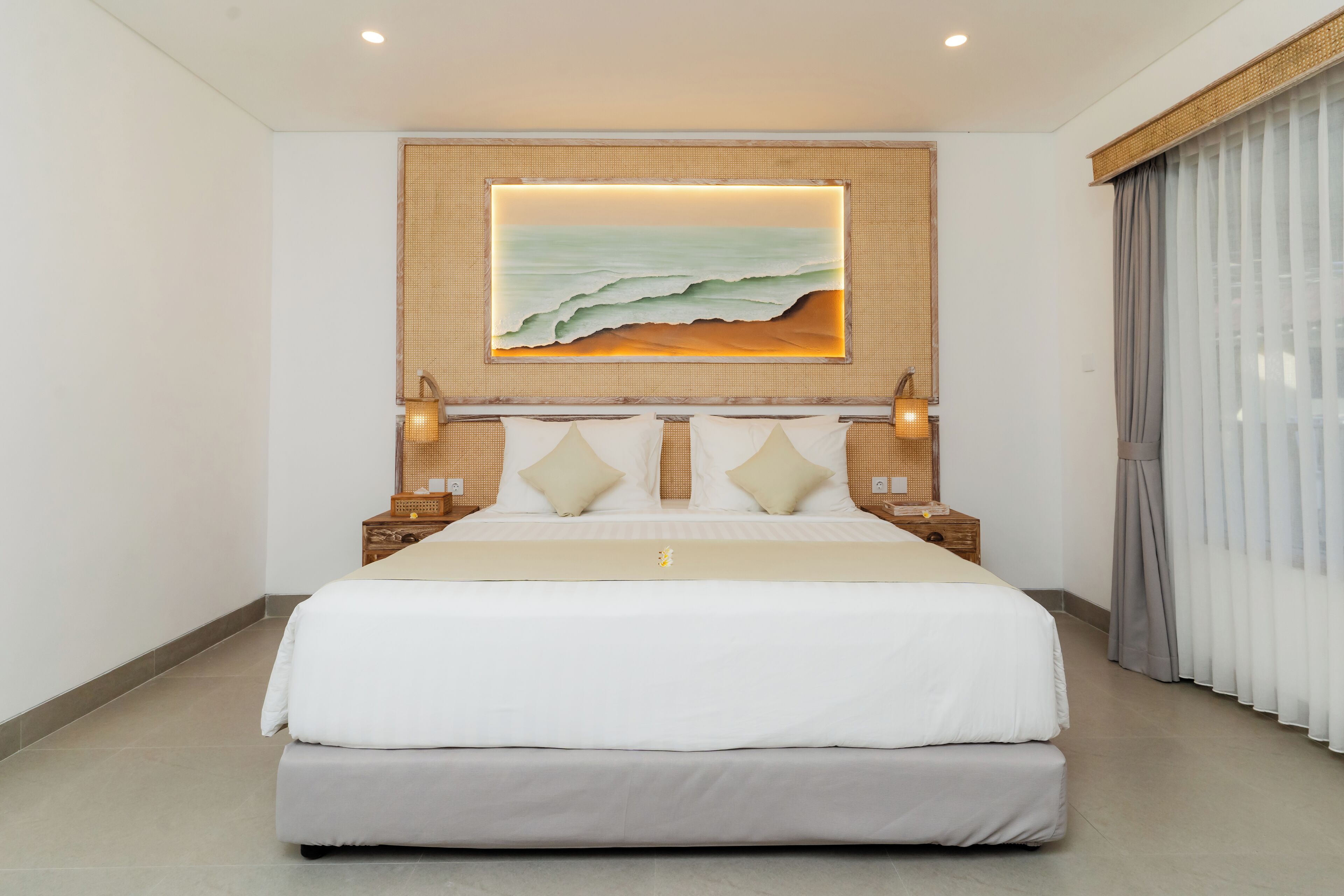 A large bed with a headboard, two bedside tables, and a wall-mounted artwork depicting a beach scene.